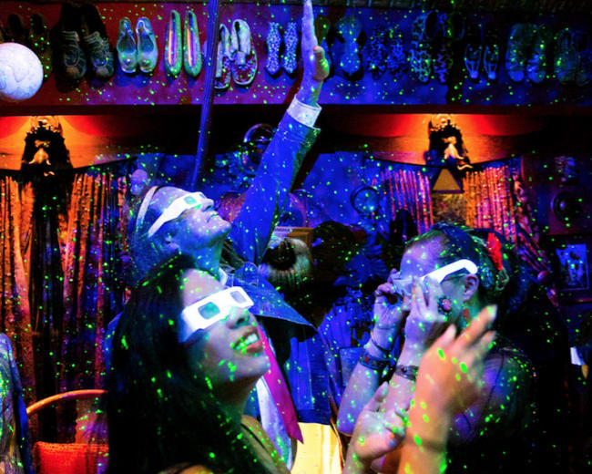 A group of people dances under multicolored lights and laser effects in a vibrant, decorated venue.