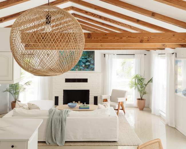 A bright living room features a white sofa, a round rattan light fixture, and large windows with sheer curtains, showcasing a cozy, open space.