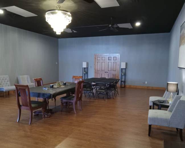 The room features a large rectangular table surrounded by chairs, with additional seating along the walls and a chandelier overhead.