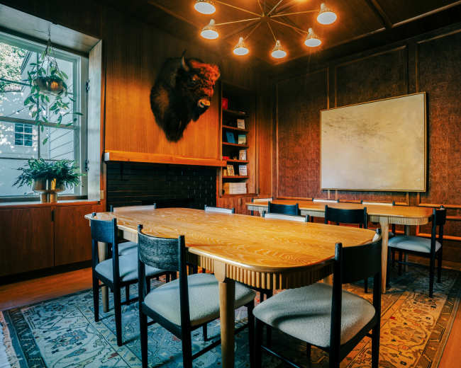 The image shows a wood-paneled conference room featuring a long wooden table with chairs, a mounted buffalo head on the wall, and a large, blank whiteboard.