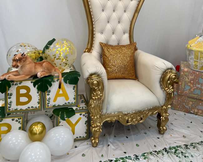 A decorated corner with a large, ornate golden chair, a "Oh Baby" backdrop, and a variety of balloons and gifts arranged for a celebration.
