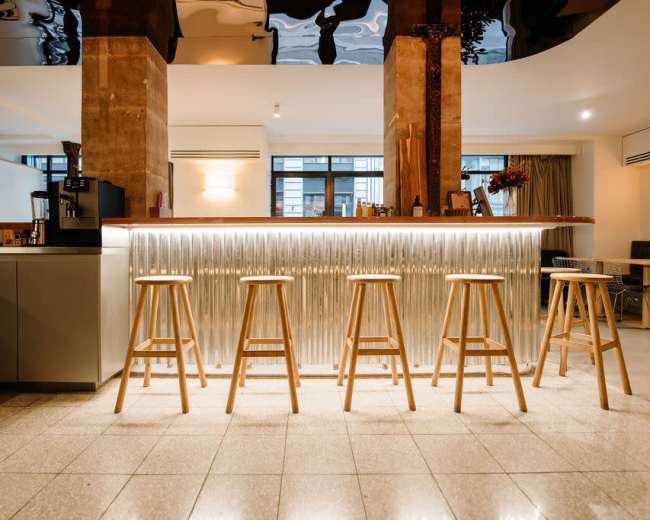 The image shows a modern bar area with a polished counter, wooden stools, and a stylish interior design featuring a reflective ceiling.