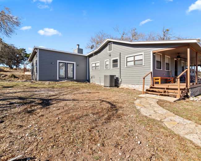 A single-story house with a covered porch and stone pathway is set on a grassy lot.