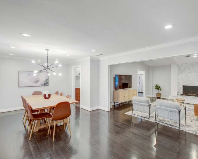 The image shows a modern, open-concept living and dining area with a wooden dining table, a cozy seating arrangement, and a fireplace.