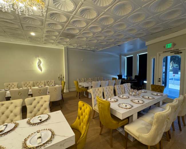 A dining room features elegant, tufted chairs and tables set with white tablecloths, ornate plates, and decorative chandeliers.