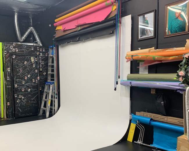 A photography studio with a white backdrop, colorful rolls of seamless paper, and various props organized on the walls and floor.