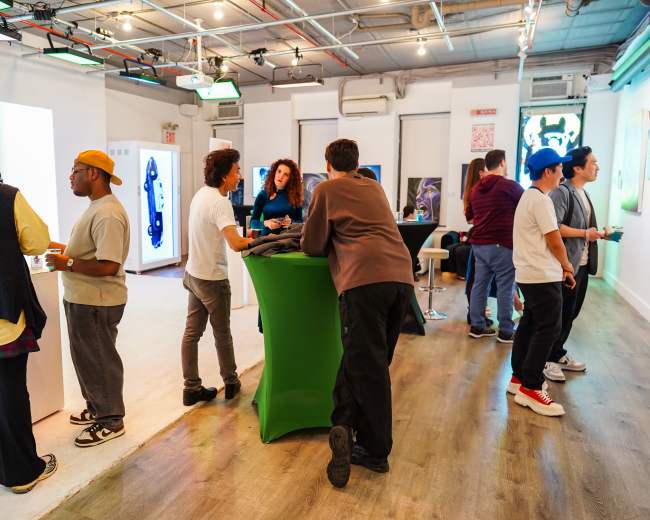 A group of people socialize and engage with displays in a modern art gallery setting.