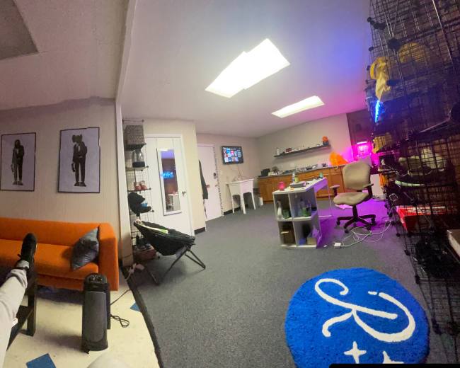 The image shows an office space with an orange couch, a desk equipped with a computer, and various items displayed on the walls and shelves.