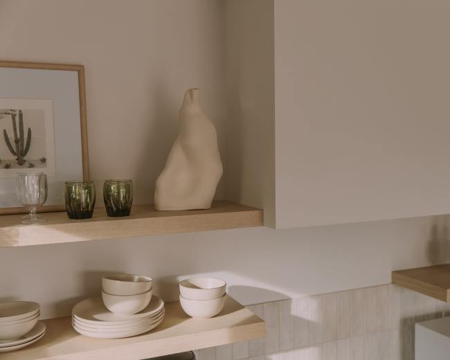 The image shows a minimalist kitchen with wooden shelves displaying various dishes, glassware, and decorative items.