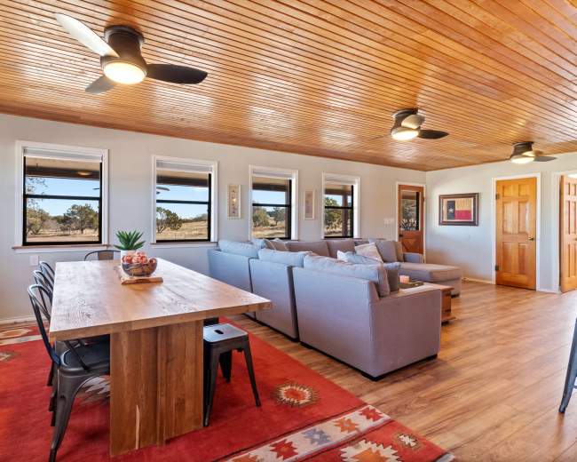 A spacious living area with a large wooden dining table, a sectional couch, and several windows allowing natural light.