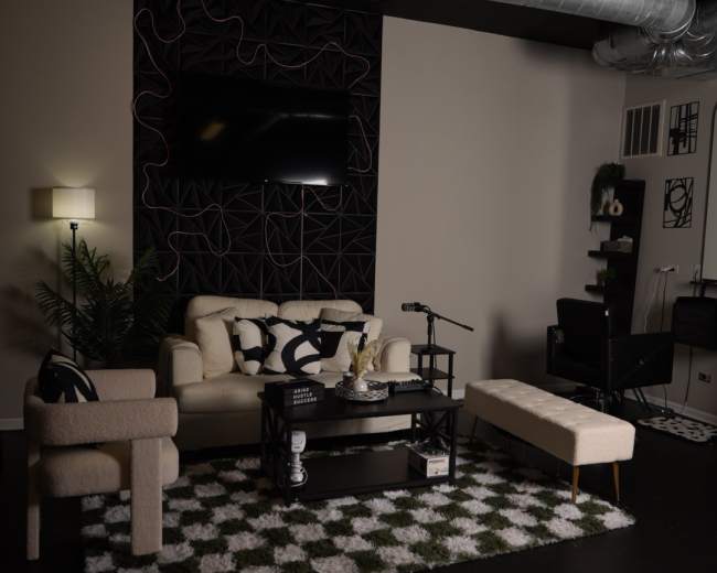 The image shows a modern living room setup featuring a sofa, a coffee table, and a patterned rug on a dark floor, with decorative elements and a television mounted on the wall.