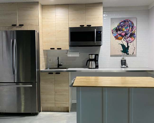 The image shows a modern kitchen with light wood cabinetry, stainless steel appliances, and a countertop island featuring a colorful rose artwork on the wall.