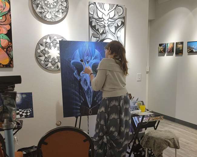 A woman is painting on a canvas in an art gallery surrounded by various artworks on the walls.