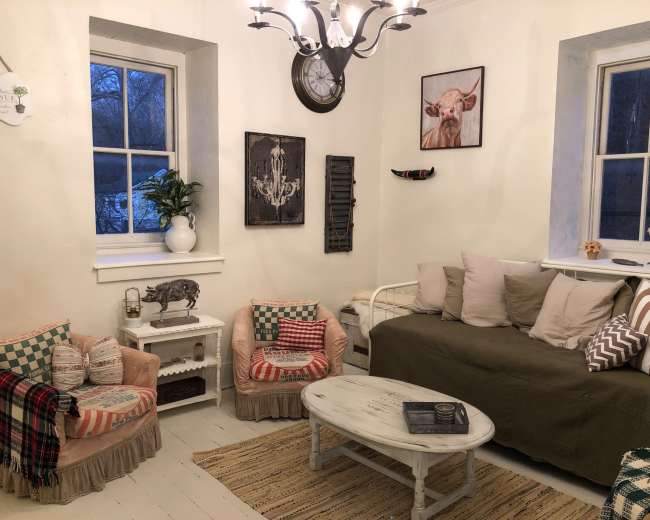 A cozy living room with a sofa, two armchairs, and a coffee table surrounded by light-colored walls and decorative wall art.