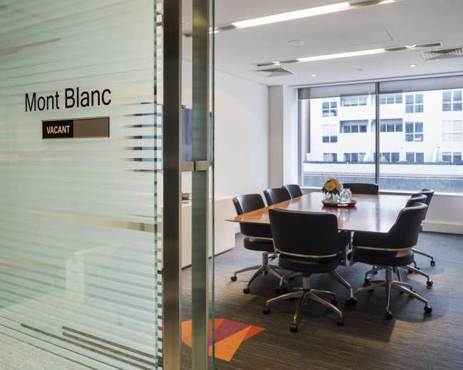 A conference room with a large wooden table and several black chairs is visible through a glass door labeled "Mont Blanc" and marked as "VACANT."