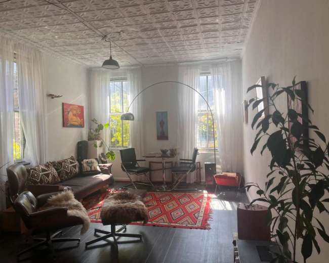 The image depicts a bright living room featuring a mix of modern and vintage furniture, with large windows allowing natural light to illuminate the space.