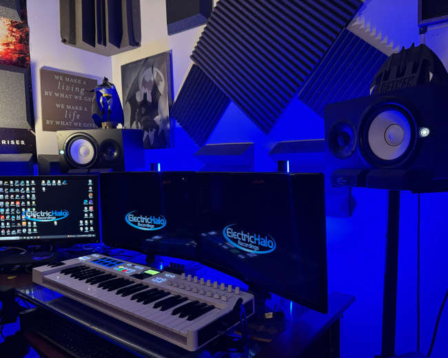 The image shows a music production setup featuring two monitors, a keyboard, and studio monitors in a room with soundproofing panels and blue lighting.