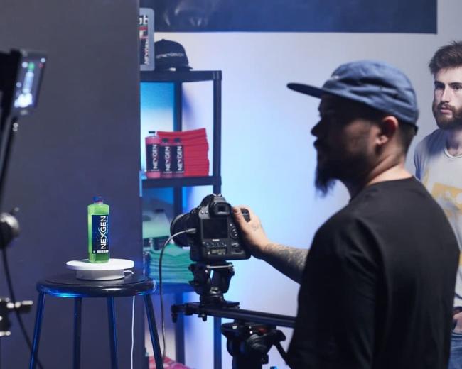 A photographer captures an image of a green bottle labeled "NEXGEN" on a table, with studio equipment and a model in the background.