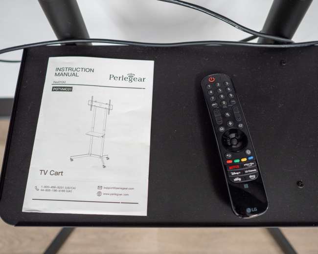 A remote control and an instruction manual for a TV cart are placed on a black table surface.