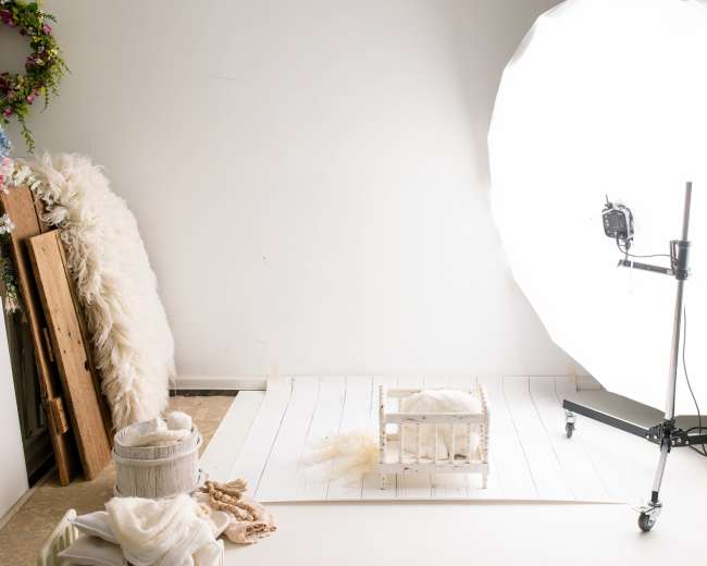 The image shows a photography studio setup with a large softbox light and a wooden crate on a white backdrop.