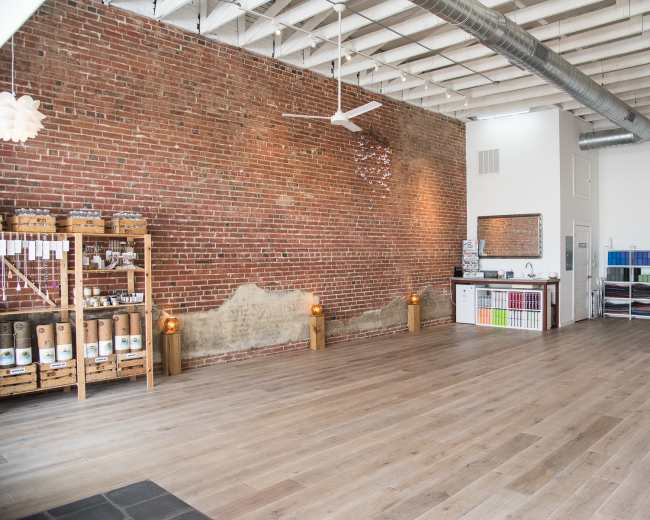 The interior of a spacious room features exposed brick walls, wooden flooring, and a well-organized area with shelving units along one side.