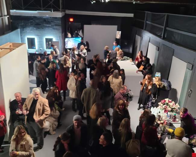A large crowd of people socializes at an indoor event space featuring tables and artworks.