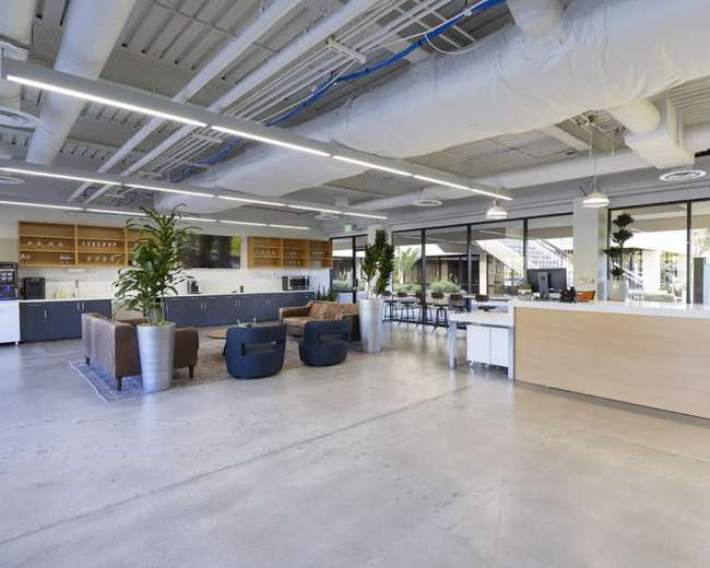 A modern office interior featuring a reception area, lounge seating, and kitchenettes, with large windows allowing natural light.
