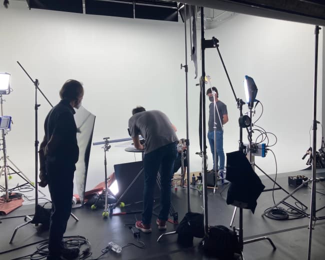 A group of people is setting up equipment in a studio with a white backdrop.