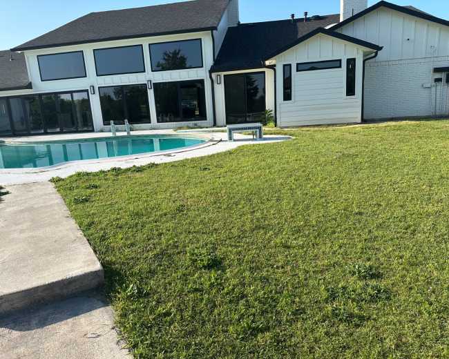 A modern house with large windows overlooks a swimming pool and a well-maintained lawn.