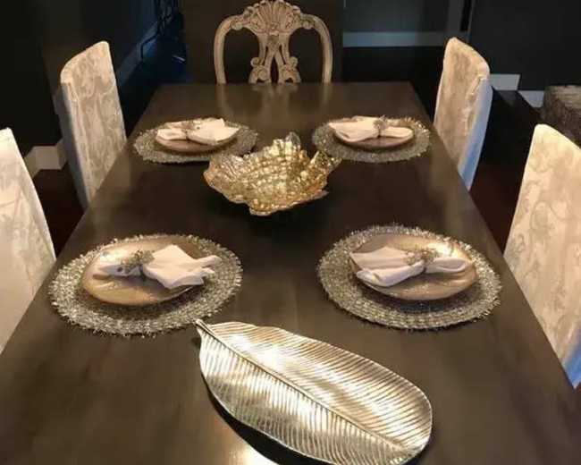 A dining table is set with decorative plates and napkins, positioned around a central ornamental bowl and a leaf-shaped dish.