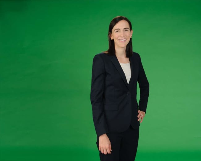 A person in business attire stands smiling against a green background.