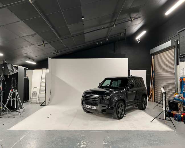 A black SUV is parked in a photography studio with a white backdrop and various equipment set around the space.