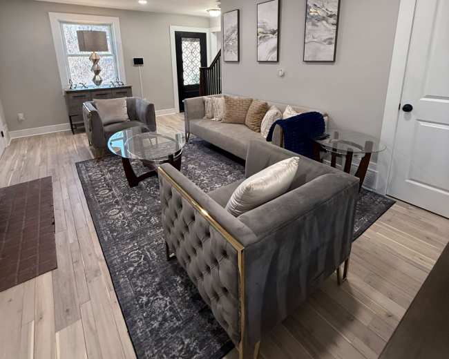 The image shows a modern living room with a gray sectional sofa, two glass-top tables, and framed artwork on the walls.