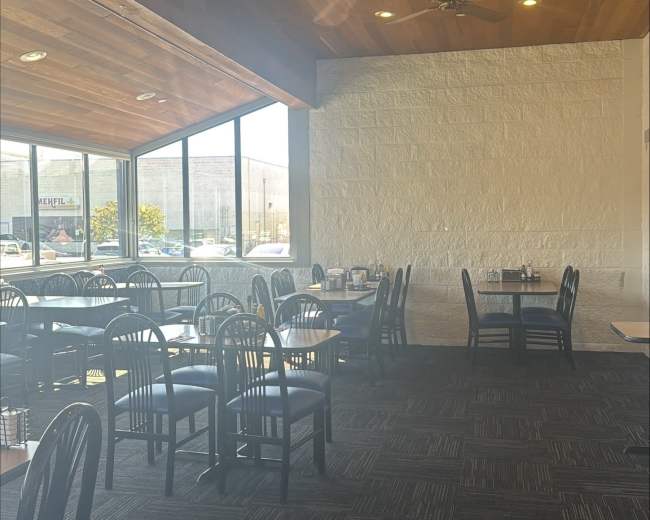 The image shows a spacious restaurant interior with black chairs and tables arranged neatly under wooden beams and ceiling fans.