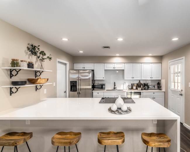 The image shows a modern kitchen with white cabinets, a large island with bar stools, and stainless steel appliances.