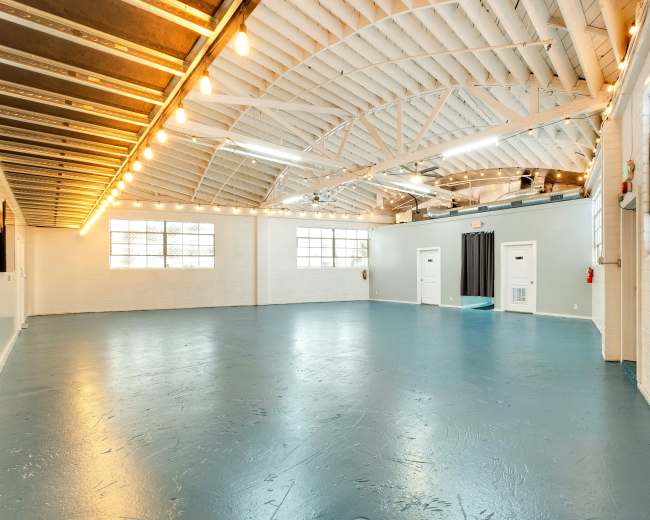 A spacious, well-lit interior with a high, arched ceiling, featuring polished blue flooring and large windows along one wall.