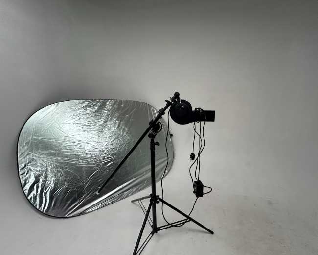 A photography setup with a silver reflector and a light mounted on a tripod.