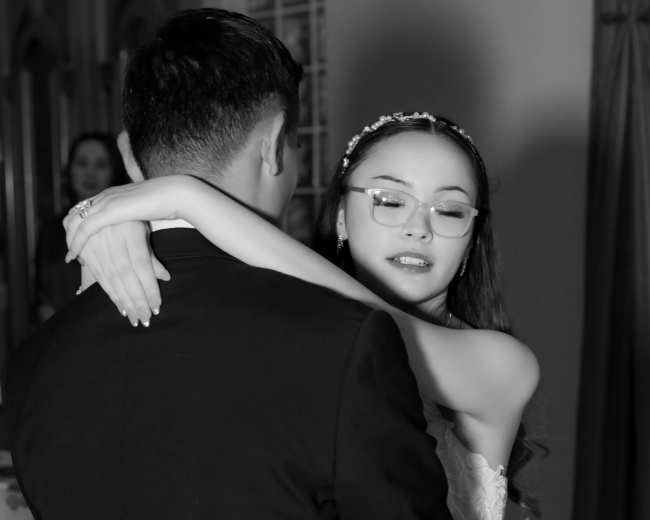 A bride in a white dress dances closely with a man in a black suit.