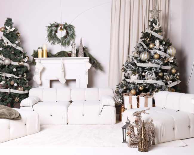 The scene features a modern living room decorated for the holidays, with two white sofas, a Christmas tree adorned with silver and gold ornaments, and a fireplace accompanied by festive decorations.