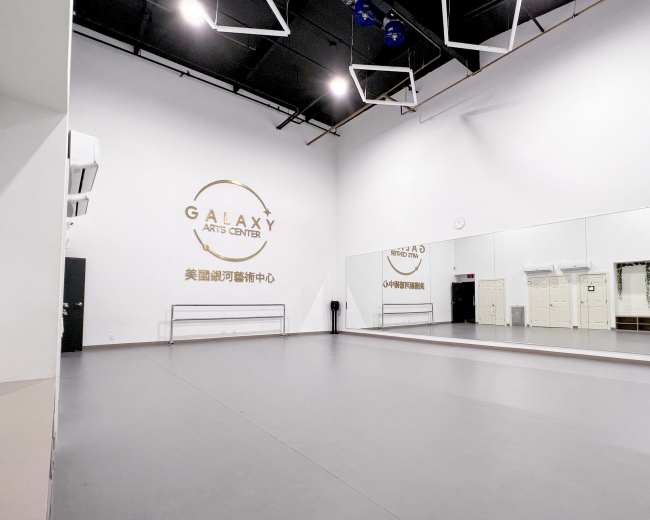 The image shows a spacious dance studio featuring a large mirrored wall and the name "GALAXY ARTS CENTER" displayed on the wall.
