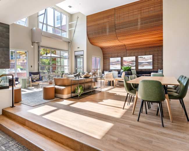 The spacious interior features large windows, a fireplace, modern seating arrangements, and a dining area with a wooden table, all set in a well-lit, contemporary design.