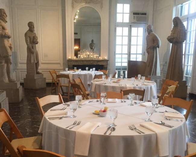 A dining room with round tables set for a meal, surrounded by large sculptures and featuring large windows that allow natural light.