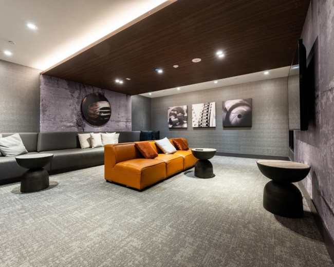 The image shows a modern lounge area with a gray sofa, an orange seating arrangement, round tables, and abstract wall art.