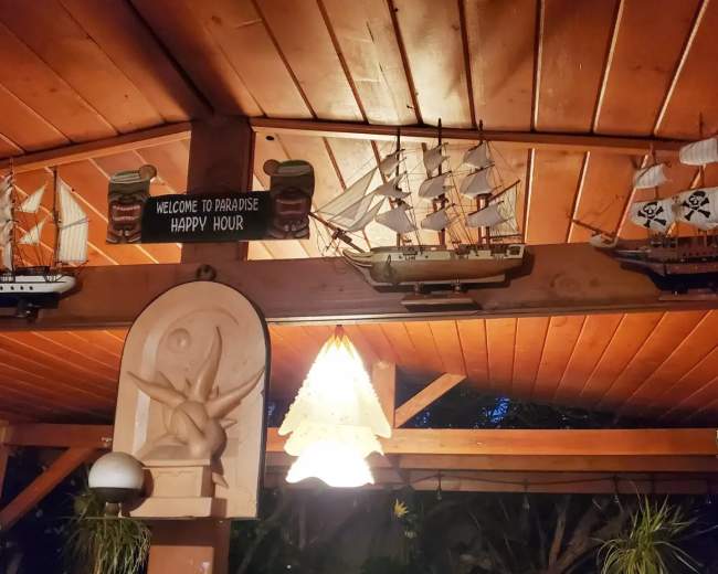 A wooden gazebo interior with decorative ship models, a welcome sign, and a hanging light fixture.