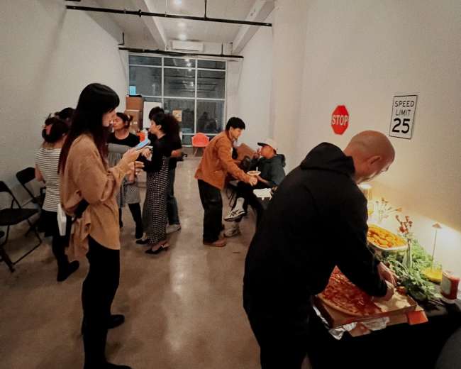 A group of people gathers in a room with a buffet table, engaging in conversation and enjoying food and drinks.