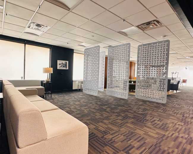 The image shows a modern office interior featuring a light-colored sofa, a lamp, and decorative partition screens, with large windows providing natural light.