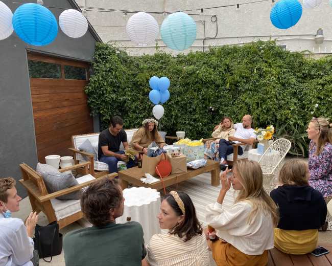 A group of people is gathered in an outdoor space decorated with lanterns, sitting near presents and refreshments.