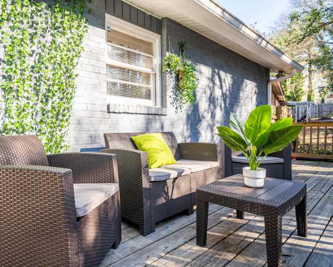 A patio area features wicker furniture with green cushions and potted plants against a gray wall.