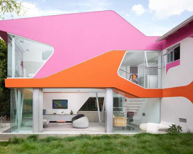 A modern house with vibrant pink and orange geometric designs on the exterior, large glass windows, and a landscaped backyard.