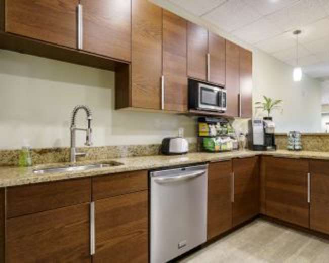 The image shows a modern kitchen featuring wood cabinetry, a stainless steel dishwasher, a microwave, and a granite countertop with a sink.